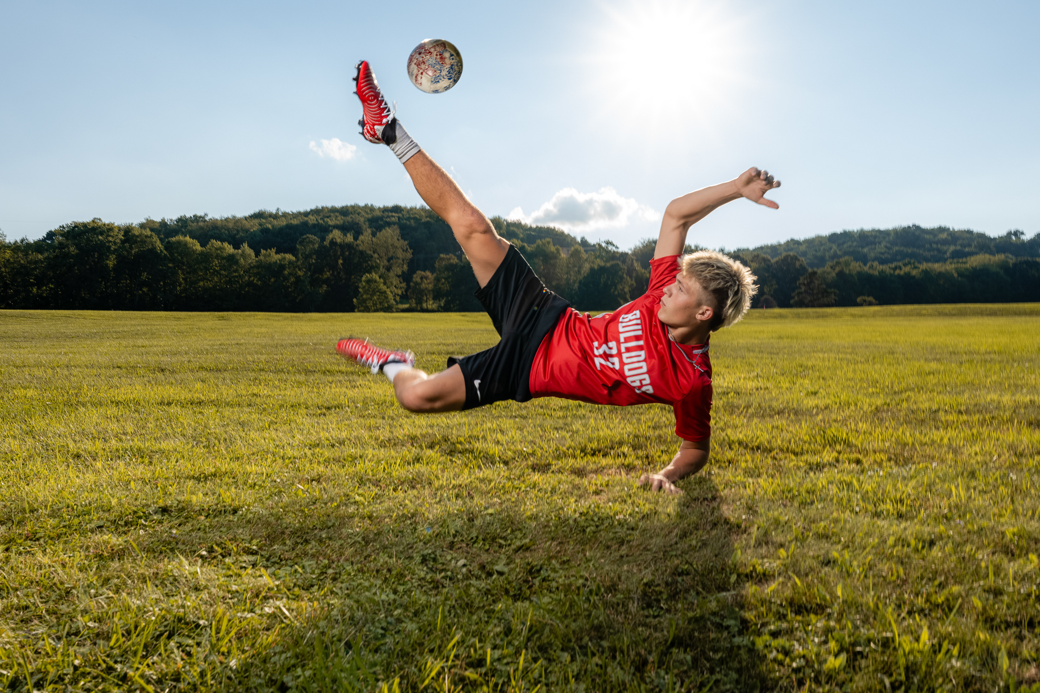 Photo by cranberry township senior photographer of a senior kicking a soccer ball mid air in a field near Cranberry Township PA